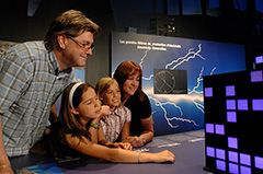 Des parents en compagnie de leurs deux filles portent attention à un des éléments de l'exposition.